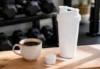 Caffeine and creatine together: a cup of black coffee beside a shaker bottle and a scoop of creatine monohydrate powder on a gym bench