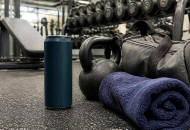 An energy drink can on a gym floor next to a kettlebell, gym bag and towel