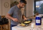 Anabolic window: man preparing a post-workout meal of eggs on toast and milk in his kitchen, with a whey protein tub and shaker on the counter